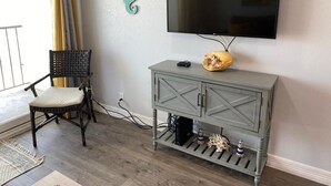 A living room with a grey cabinet, a black TV, a wicker chair, and a teal seahorse decoration. - Oceanview Beach Getaway, Great balcony!! (Galveston)