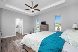 Une chambre à coucher avec un lit, un ventilateur de plafond, une commode et un téléviseur.