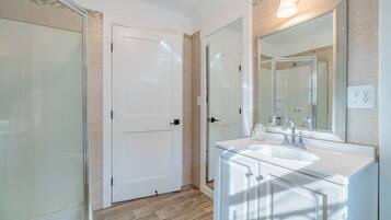 A bathroom with a glass shower enclosure, a white sink with a mirror above it, and a door with a handle.