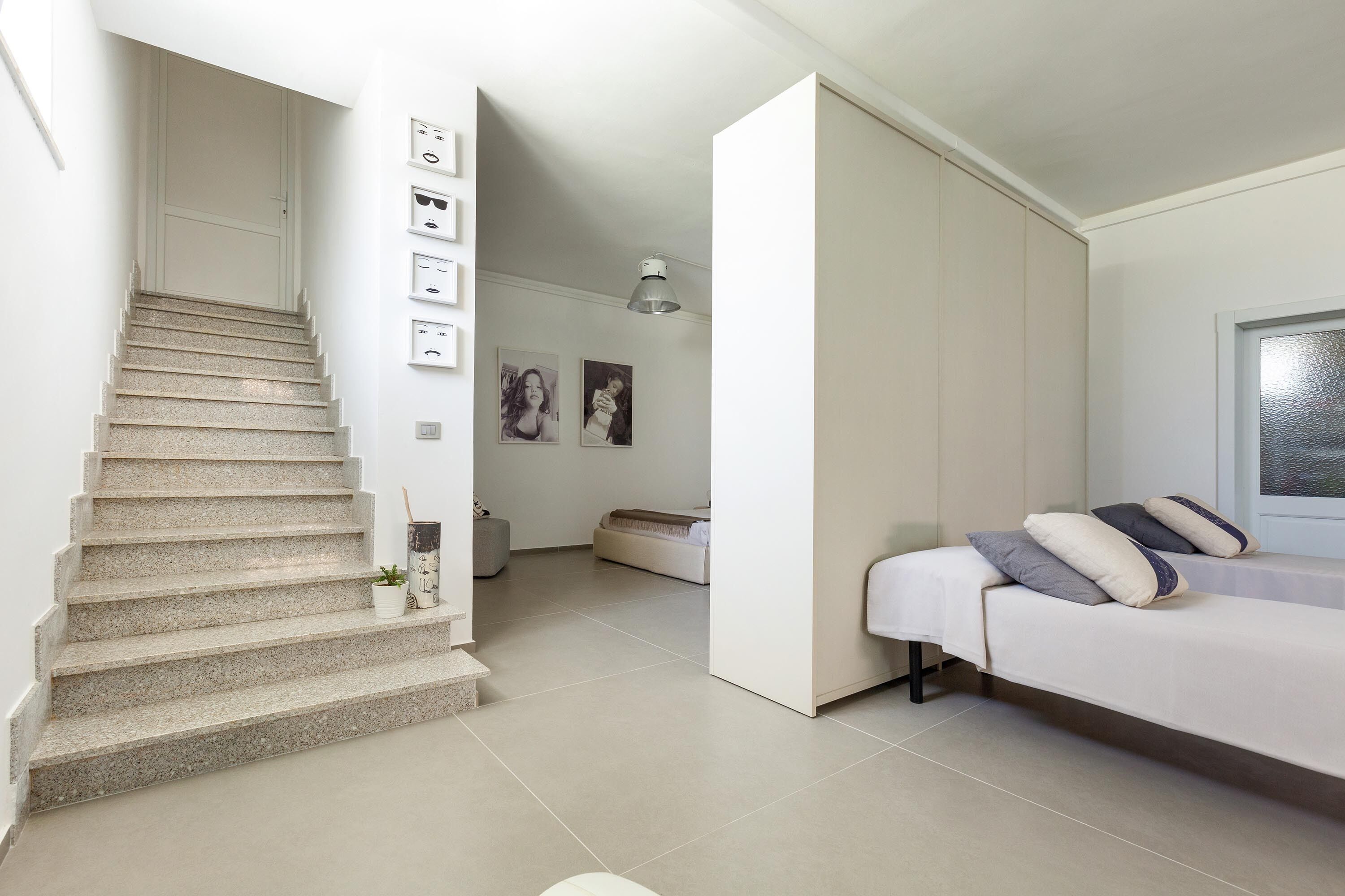 Ein modernes Schlafzimmer mit Bett, Nachttisch, Fenster und einer Treppe, die in einen anderen Raum führt.