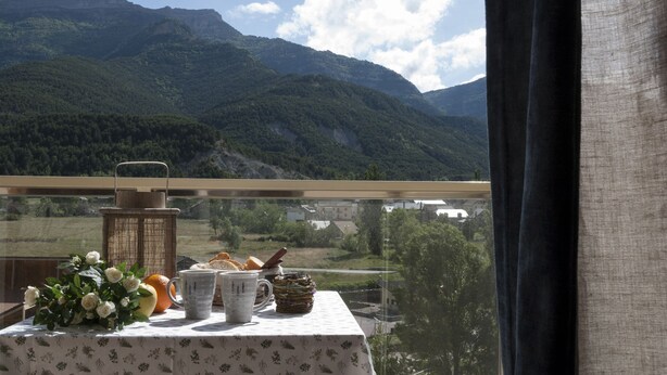 A table with a floral tablecloth, white cups, a basket, and bread on a balcony with a mountain view. - Hostal Rio Ara Bellosta (Fiscal)