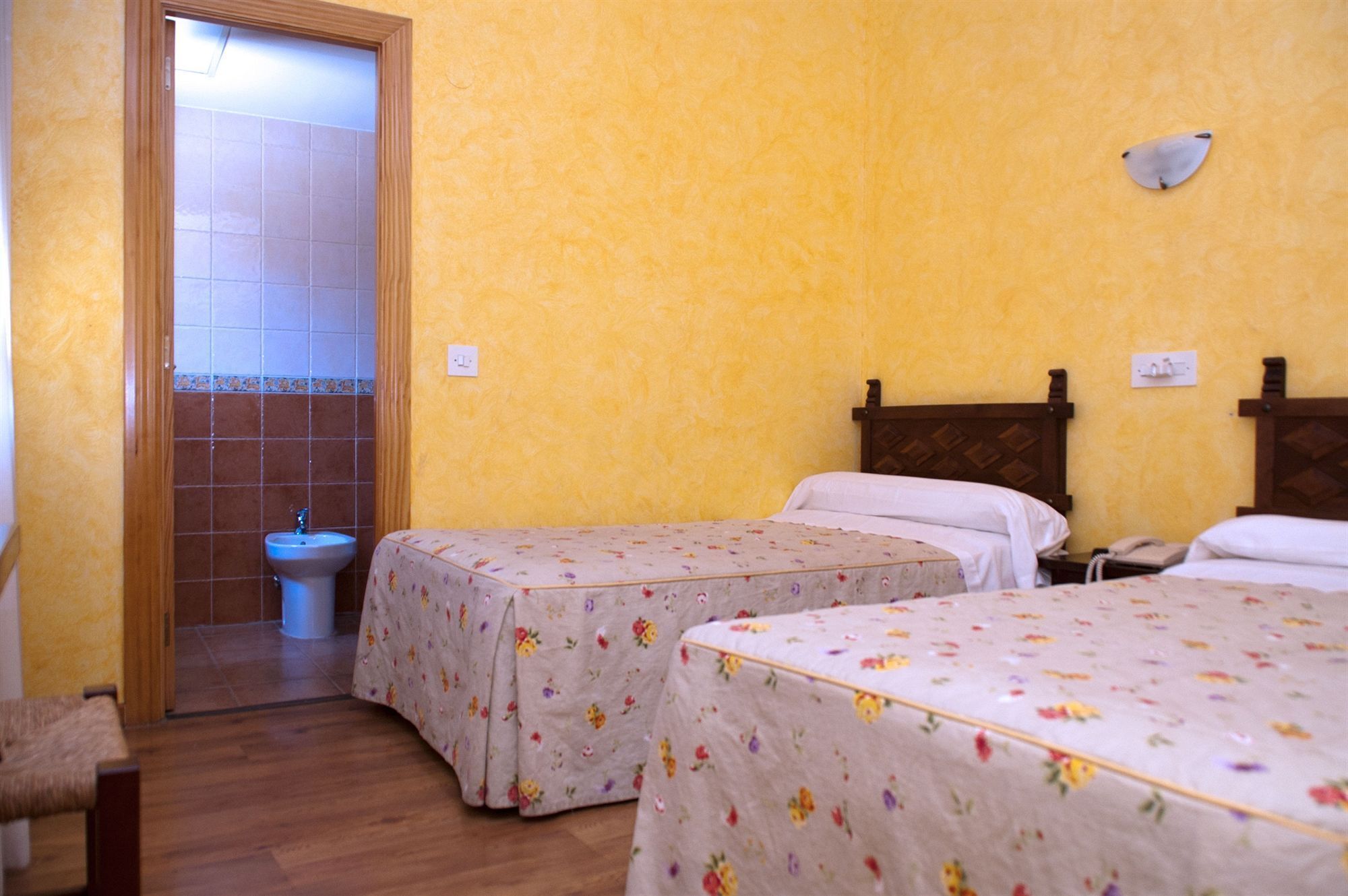 Una habitación con dos camas, una puerta de madera, un lavabo y un enchufe.