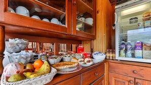 A wooden kitchen counter with various food items, a refrigerator, and a basket of fruits. - Hostal Rio Ara Bellosta (Fiscal)