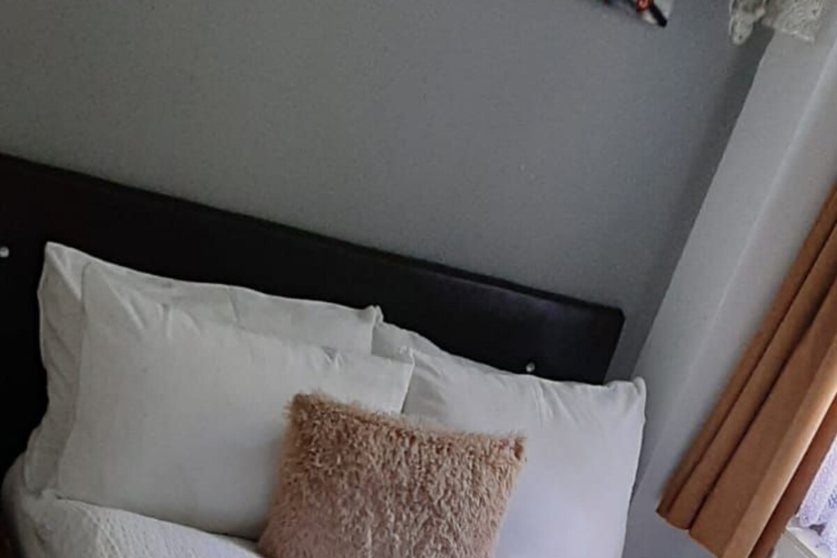 A neatly made bed with white bedding, a beige pillow, and a rolled towel.