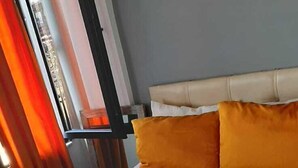 A neatly made bed with white and orange bedding, a headboard, and a window with curtains. - Dolapdere Zona Apart (Istanbul)