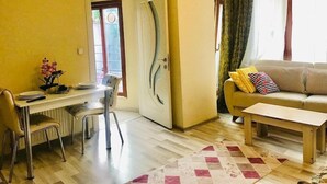 A living room with a sofa, a coffee table, a dining table with chairs, and a door leading to an outdoor area. - Dolapdere Zona Apart (Istanbul)