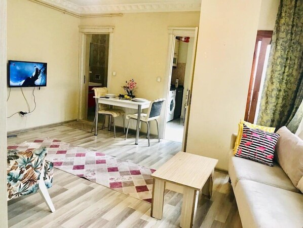 A living room with a sofa, a coffee table, a TV, a dining area with a table and chairs, and a kitchen visible through an open door. - Dolapdere Zona Apart (Istanbul)
