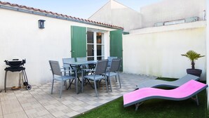 Une terrasse avec une table et des chaises, un barbecue et deux fauteuils de jardin.