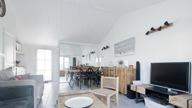 Un salon spacieux avec une grande télévision, un coin repas avec des chaises et une cuisine à l’arrière-plan.