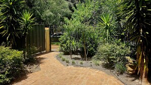 Ein gepflasterter Gartenweg, umgeben von üppigem Grün und einem hölzernen Tor.