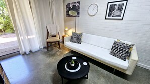 Ein modernes Wohnzimmer mit einem weißen Sofa, gemusterten Kissen, einem kleinen runden schwarzen Couchtisch und einem Beistelltisch mit einer Lampe.