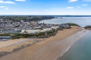Vue aérienne d’une ville côtière avec une plage de sable, une église imposante et un château perché sur une colline.