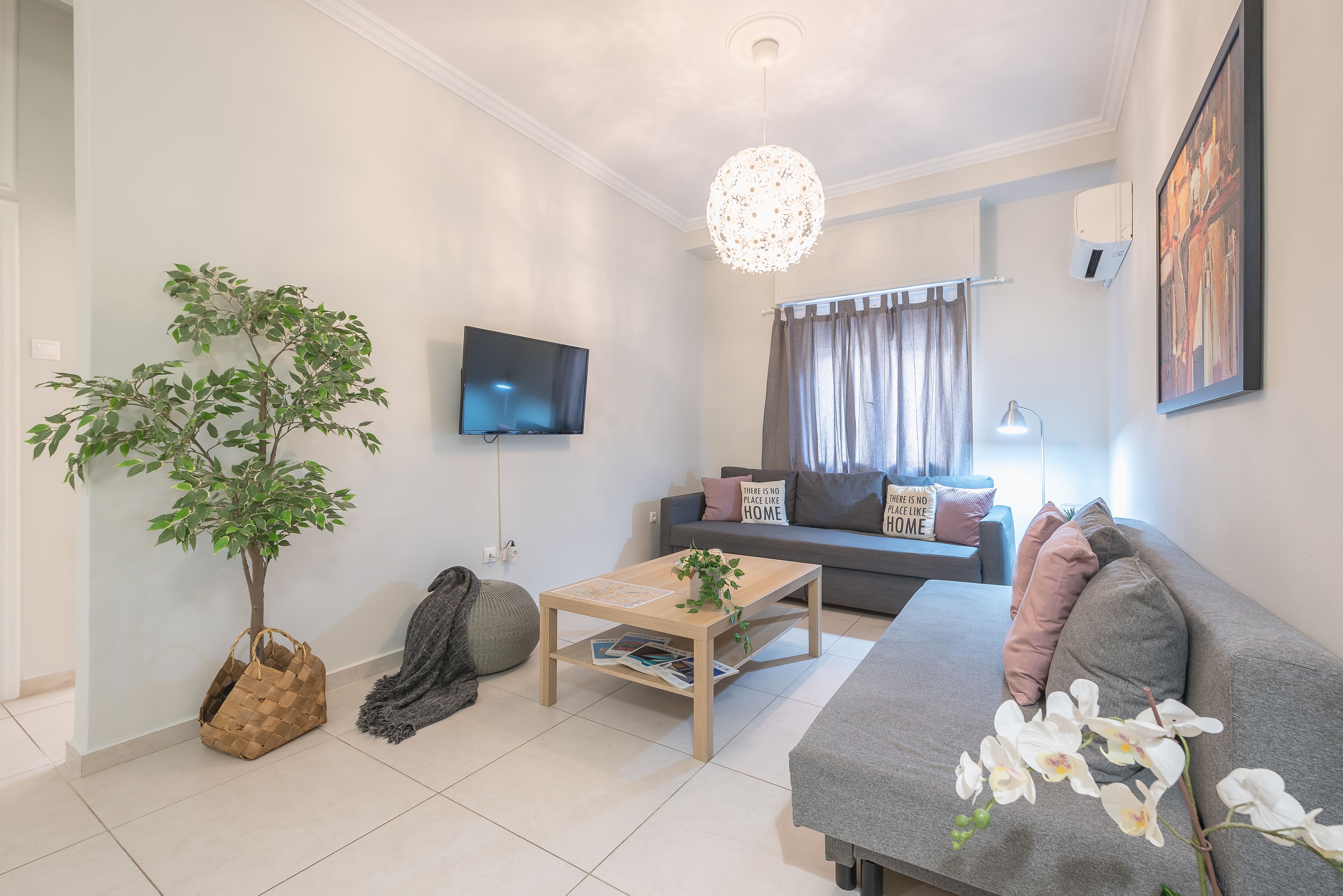 A modern living room with a sofa, a coffee table, a TV, a plant, and a decorative light fixture.