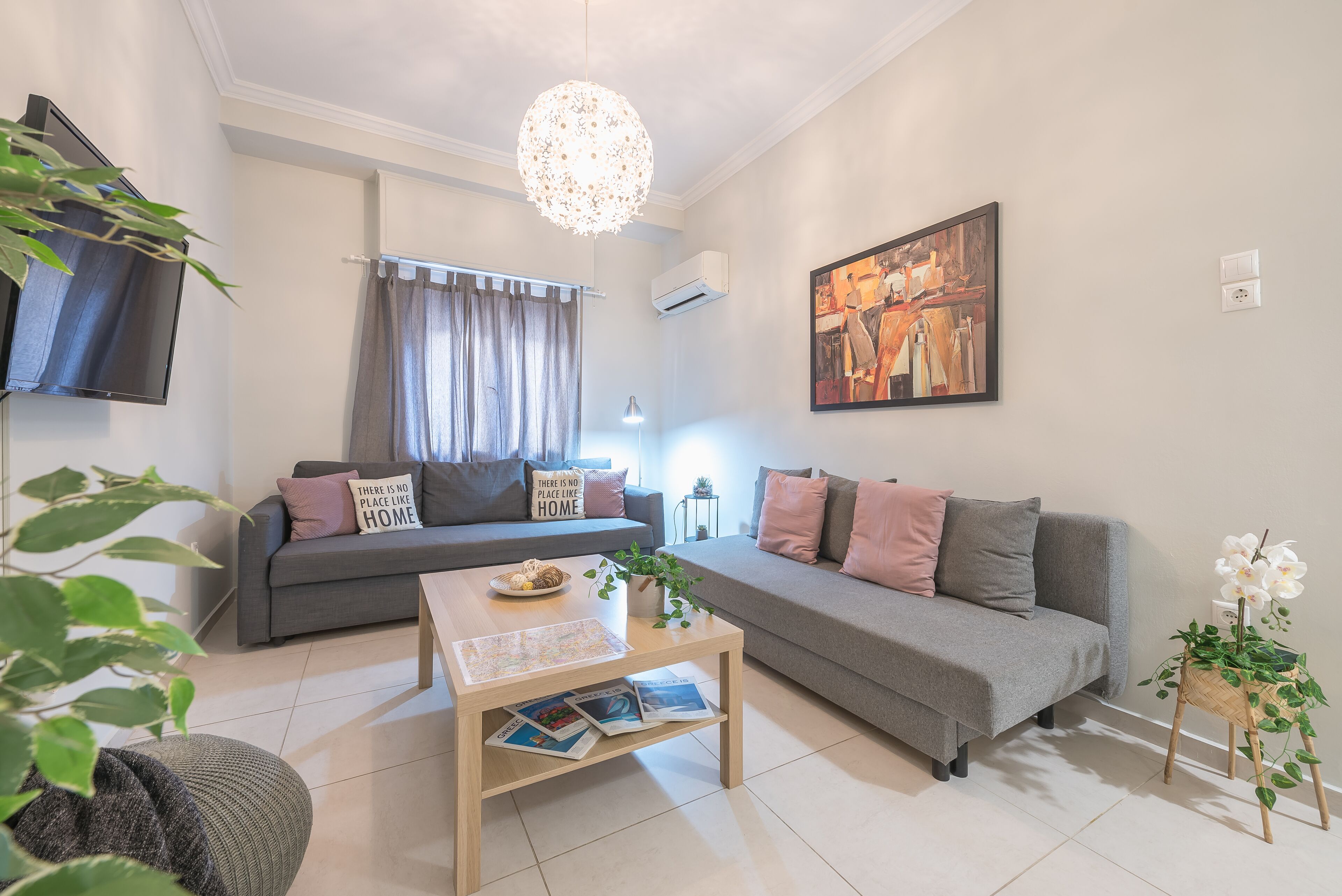 A modern living room with a grey sofa, a coffee table with magazines, a hanging light fixture, and a painting on the wall.