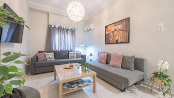 A modern living room with a grey sofa, a coffee table with magazines, a hanging light fixture, and a painting on the wall.