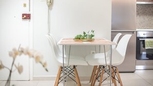 A modern kitchen with white cabinetry, a stainless steel oven, and a dining area with a white table and chairs.