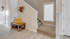 A staircase with a carpeted landing, a bench with a yellow cushion, and a wall-mounted shelf with books and a small plant. - Revival on The Park (Calgary)