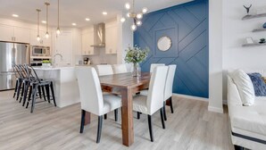 A modern kitchen with white cabinets, a wooden dining table, and a blue accent wall. - Revival on The Park (Calgary)