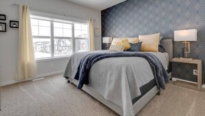 A bedroom with a large bed, a nightstand, a lamp, and a view through a window. - Revival on The Park (Calgary)