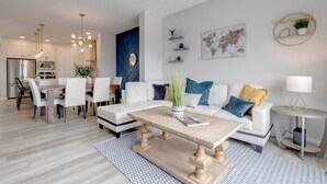 A modern living room with a dining area, white sofas, a coffee table, and a world map on the wall. - Revival on The Park (Calgary)