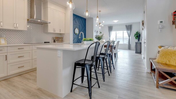 A modern kitchen with white cabinets, a central island, and black bar stools. - Revival on The Park (Calgary)