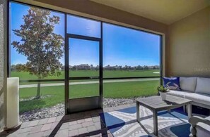 Relax in this serene room with a sofa, coffee table, and potted plant, leading to an outdoor space with a lawn and golf course views.