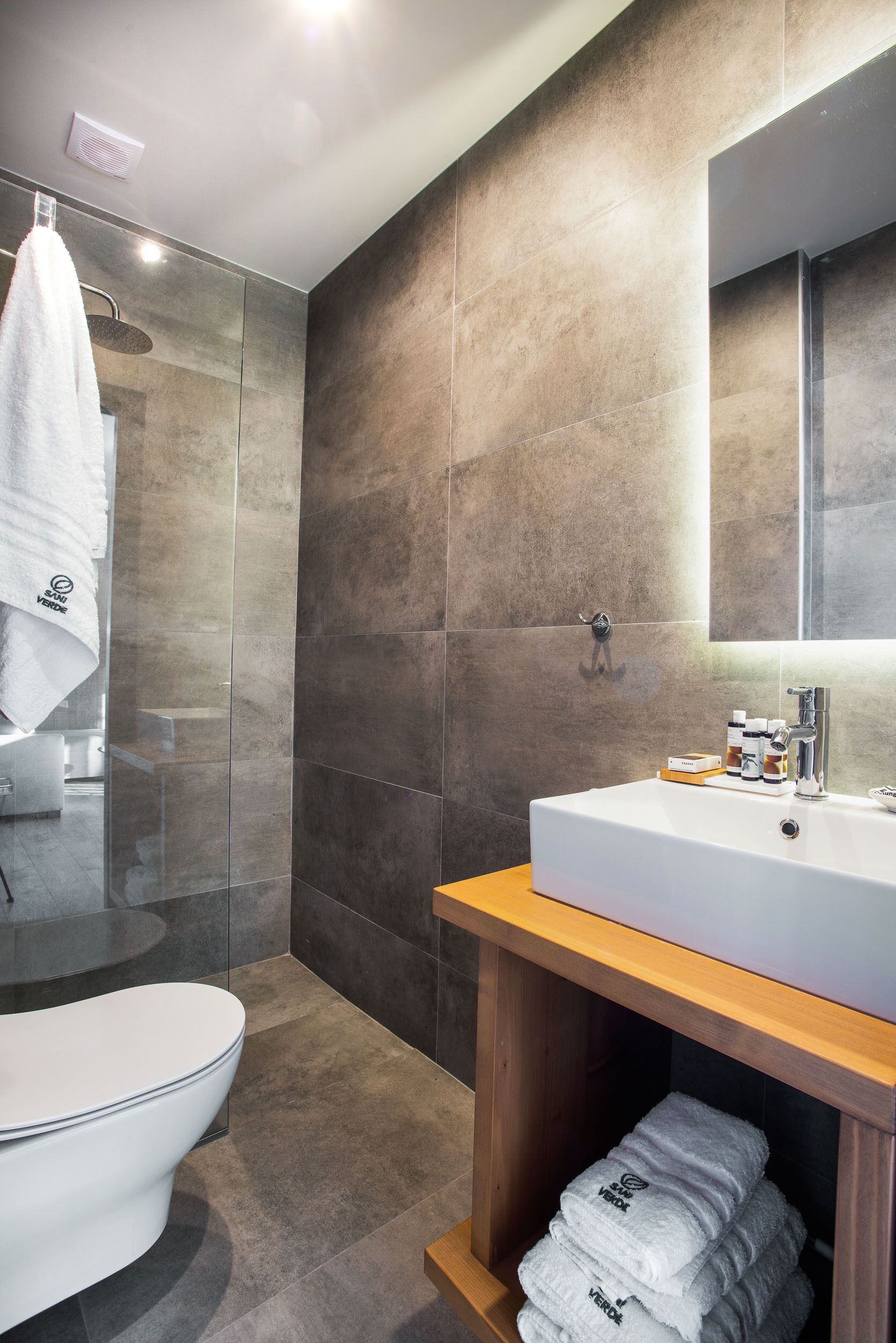 Un baño moderno con inodoro blanco, ducha envuelta en vidrio y tocador de madera con espejo.