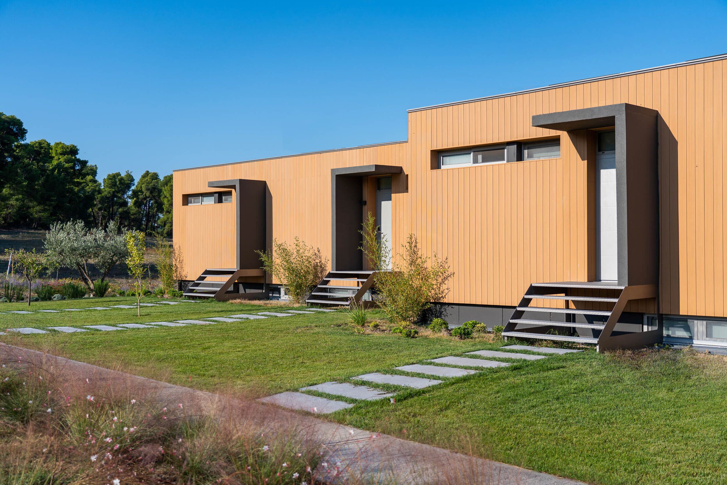A modern building with a flat roof, large windows, and a well-maintained lawn with stepping stones.