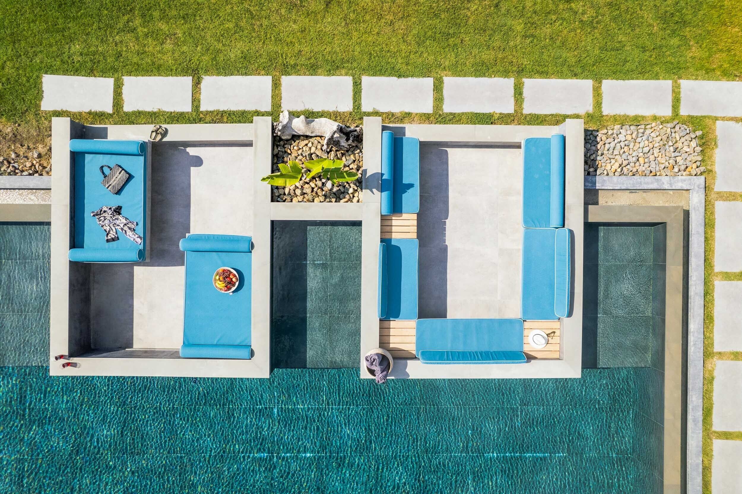 An aerial view of a swimming pool area with two separate sections, each with lounge chairs and a small table.