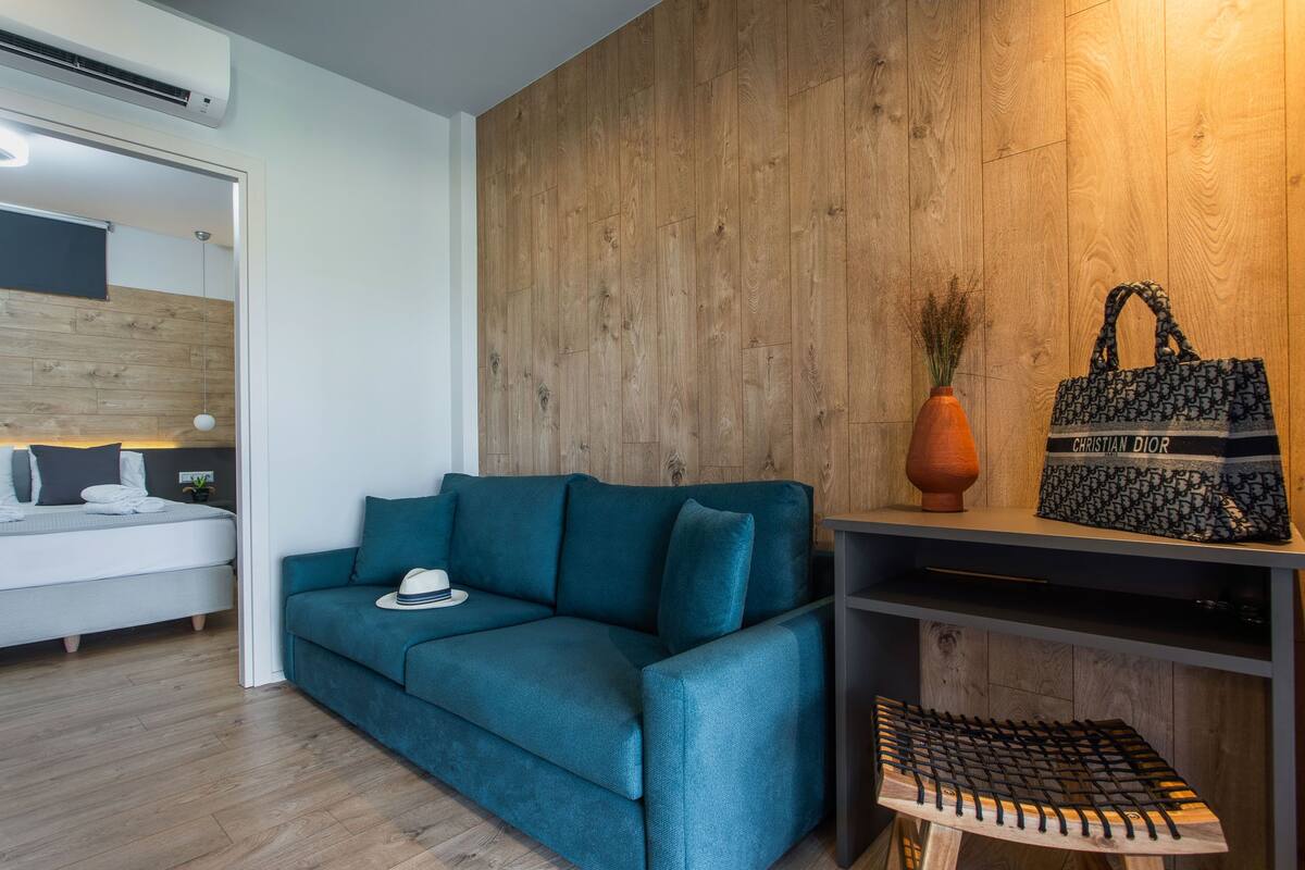 Ein modernes Zimmer mit einem salbeingrünfarbenen Sofa, einer Holzvertäfelung, einem kleinen Tisch mit einer Vase und einer Handtasche auf einem Regal.