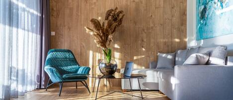 A modern living room with a wooden floor, a blue armchair, a grey sofa, a glass coffee table, and a laptop.
