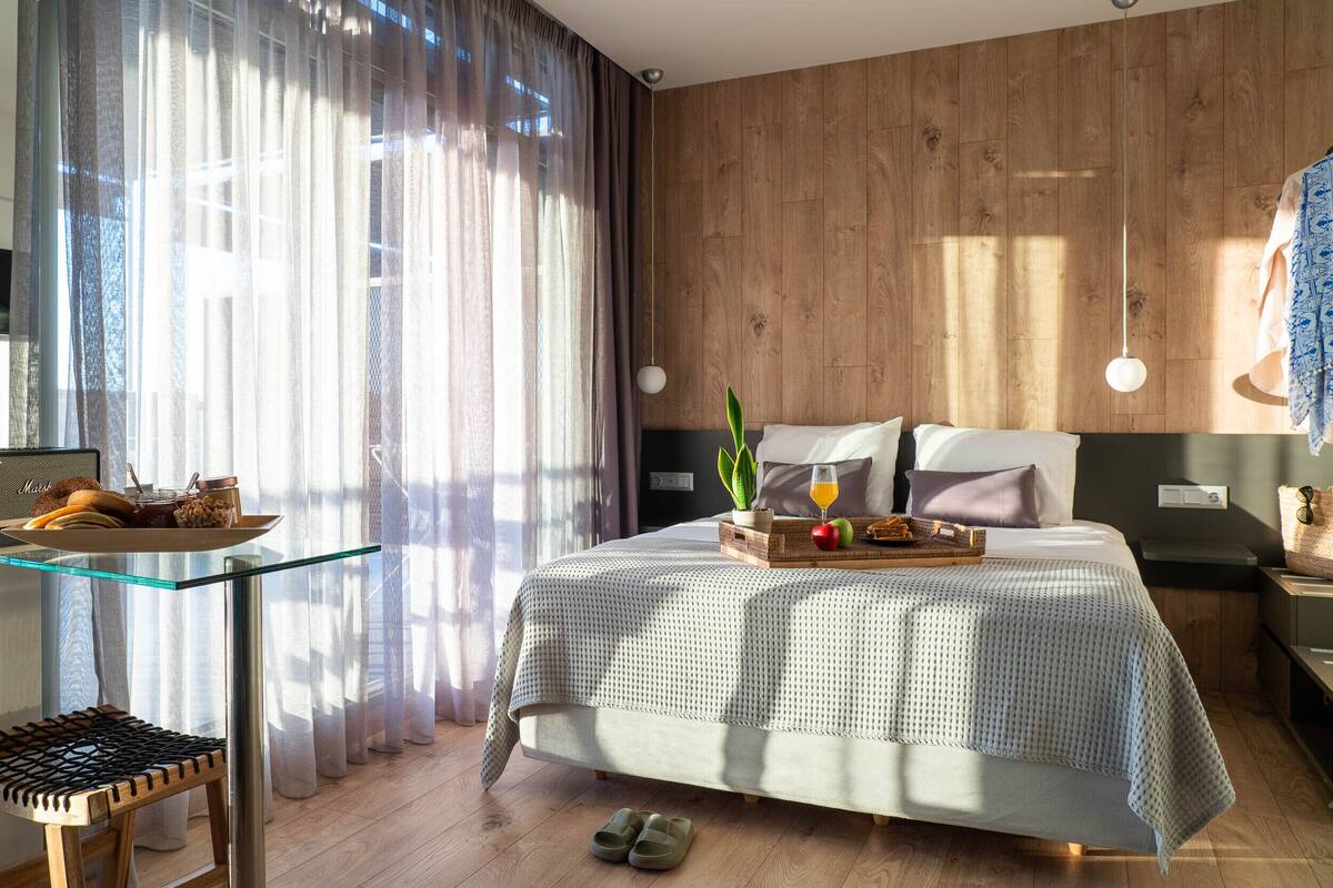 Ein modernes Schlafzimmer mit Glastisch, Bett mit Obstkorb und Pflanze, Holzwänden und Blick ins Freie.