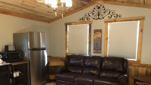 Interior acolhedor de uma cabana com cozinha compacta, um sofá de couro, piso de madeira e um objeto decorativo na parede.