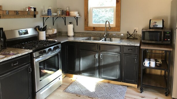 A modern kitchen with stainless steel appliances, wooden beams, and a window providing natural light. - Magnolia Cabin (Johnson City)