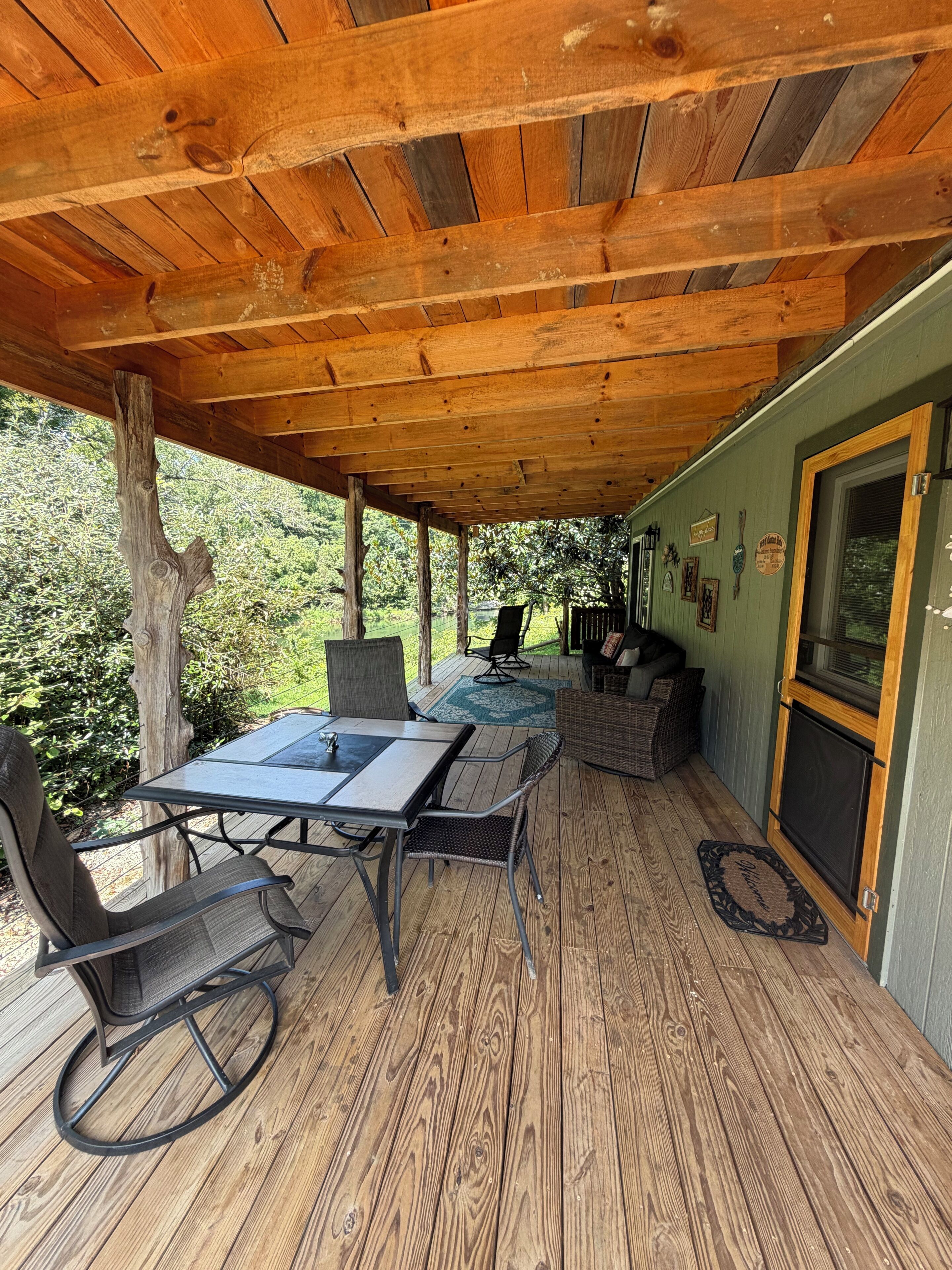 A covered patio with a table and chairs, a wicker sofa, and a grill area.