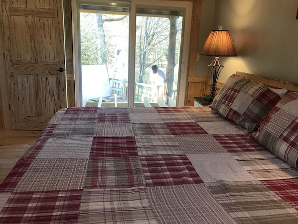 A bedroom with a large bed, a wooden door, a view of a balcony, and a lamp on the nightstand.