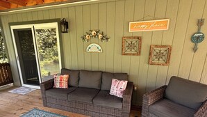 A covered porch with wicker furniture, a blue patterned rug, and decorative wall art. - Magnolia Cabin (Johnson City)
