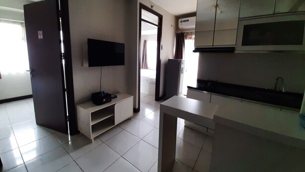 A modern kitchen with white cabinets, a built-in microwave, and a flat-screen TV mounted on the wall. - Comfortable and Cozy Living 2BR at Lagoon Apartment (Bekasi)