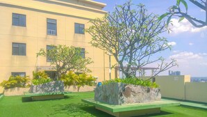 A rooftop garden with artificial grass, two large planters, and a building in the background. - Comfortable and Cozy Living 2BR at Lagoon Apartment (Bekasi)