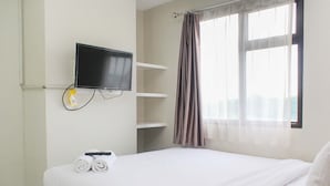 A hotel room with a bed, a TV mounted on the wall, and a window with curtains. - Comfortable and Cozy Living 2BR at Lagoon Apartment (Bekasi)