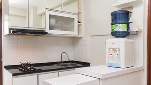 A kitchen with a gas stove, sink, white cabinets, a microwave, and a water dispenser. - Comfortable and Cozy Living 2BR at Lagoon Apartment (Bekasi)