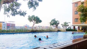 A swimming pool with people swimming, surrounded by buildings and trees. - Comfortable and Cozy Living 2BR at Lagoon Apartment (Bekasi)