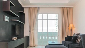 A modern living room with a flat-screen TV, a sofa, a coffee table, and a balcony with curtains. - Fully Furnished with Cozy Design 2BR The Bellezza Apartment (Jakarta)