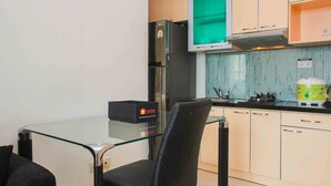 A compact kitchen with a glass-top table, a black chair, a refrigerator, a microwave, and a toaster. - Fully Furnished with Cozy Design 2BR The Bellezza Apartment (Jakarta)