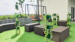 A rooftop garden with artificial grass, wicker furniture, and potted plants. - Comfort and Cozy Studio Apartment at B Residence (Pagedangan)
