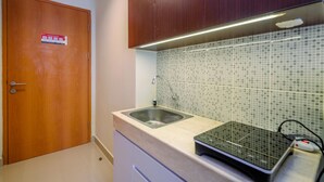 A kitchen with a wooden door, a tiled backsplash, a sink, and a microwave. - Restful and Tidy Studio at Evenciio Margonda Apartment (Depok)