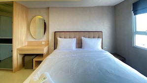 Ett modernt hotellrum med en säng, ett sängbord, en spegel och ett fönster.