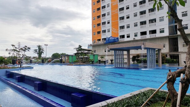 A swimming pool with a water fountain, surrounded by greenery and a multi-story building with balconies. - Best Deal and Comfort Big Studio at Green Pramuka City Apartment (Jakarta)