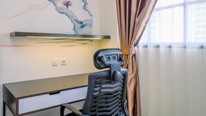 A modern office chair with a headrest, a desk with a drawer, and a wall with a painted abstract design. - Cozy Stay and Tidy Studio at Evenciio Margonda Apartment (Depok)