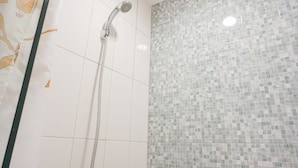 Ducha con manguera de mano y pared de azulejos con diseño de mosaico.